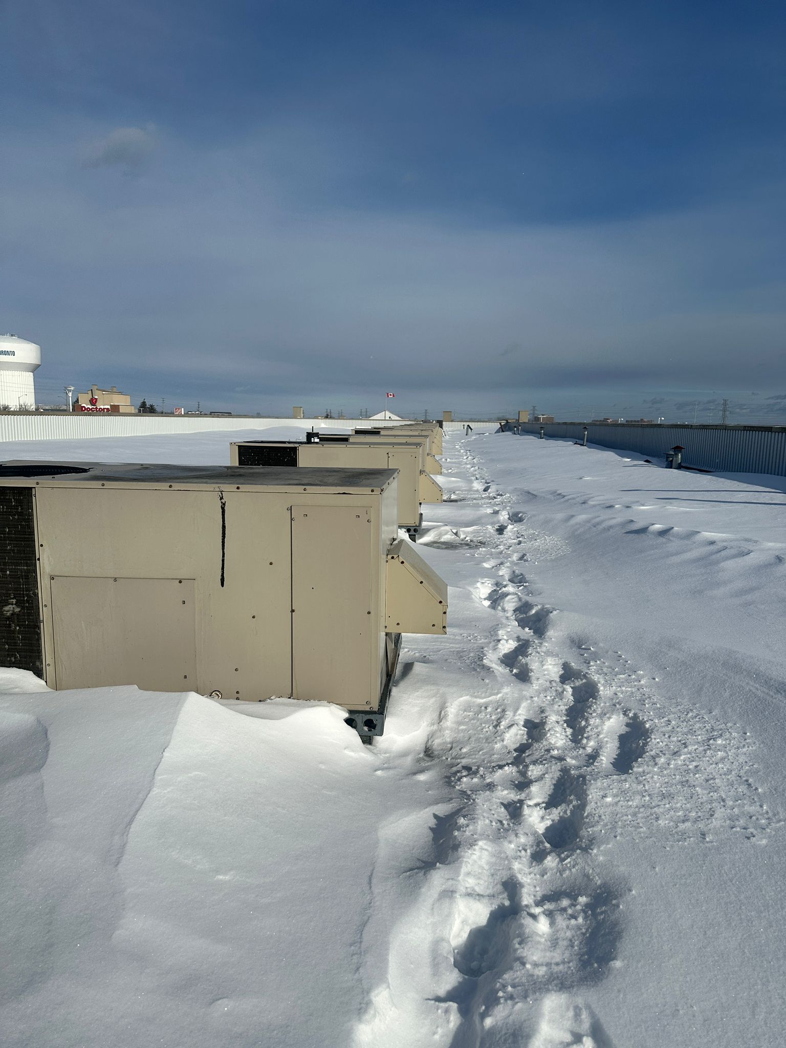 Technician footprints in snow leading to commercial rooftop HVAC units during winter service call in Oshawa